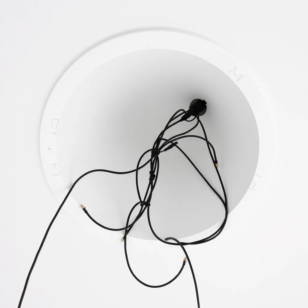 Black and white electrical wires hanging out of a freshly cut circular hole in a drywall ceiling.